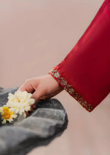 Khizra Artstyle cherry-red embroidered 3-piece suit — Gul Naaz design, close-up of the gold-embroidered cuff, hand reaching for flowers on a stone fountain